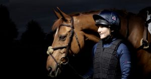 Photo of a lady dressed in riding gear, standing next to a horse.